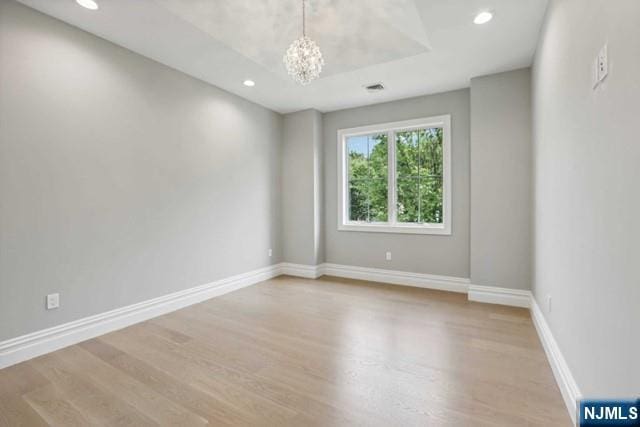 unfurnished room featuring wood-type flooring, a chandelier, and a tray ceiling