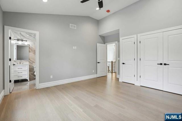 unfurnished bedroom featuring lofted ceiling, connected bathroom, light hardwood / wood-style floors, and ceiling fan