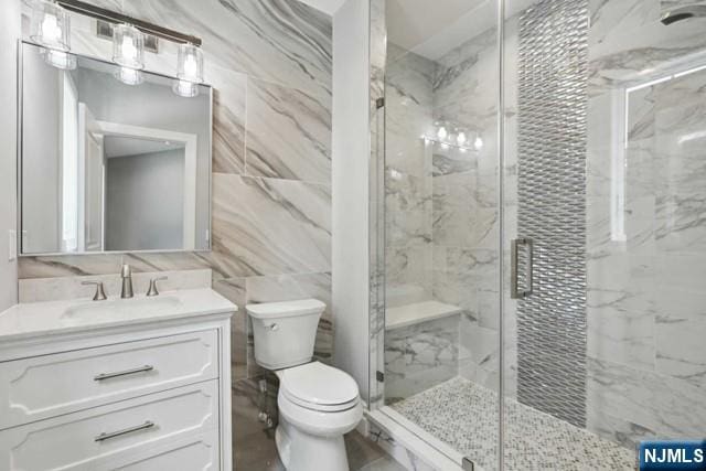 bathroom featuring vanity, toilet, a shower with door, and tile walls