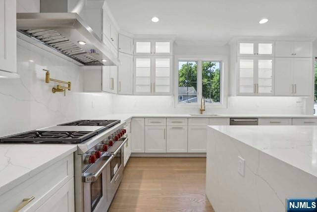 kitchen with sink, appliances with stainless steel finishes, light stone counters, white cabinets, and wall chimney exhaust hood