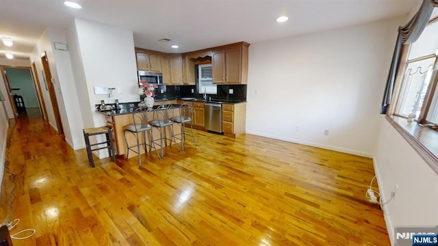 kitchen with light hardwood / wood-style floors, appliances with stainless steel finishes, decorative backsplash, a breakfast bar, and sink