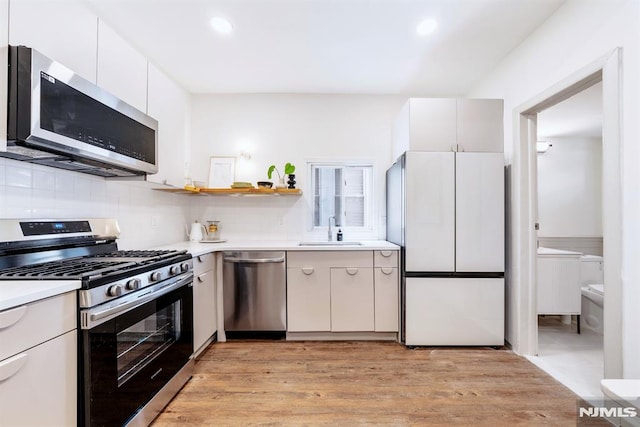 kitchen featuring white cabinets, stainless steel appliances, decorative backsplash, sink, and light wood-type flooring