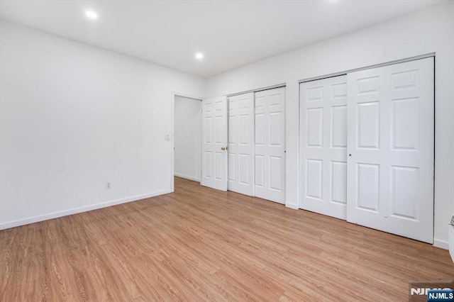 unfurnished bedroom featuring multiple closets and light hardwood / wood-style floors