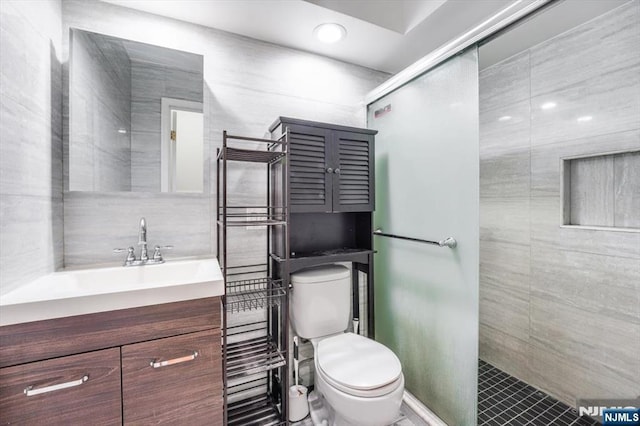 bathroom featuring tiled shower, vanity, toilet, and tile walls