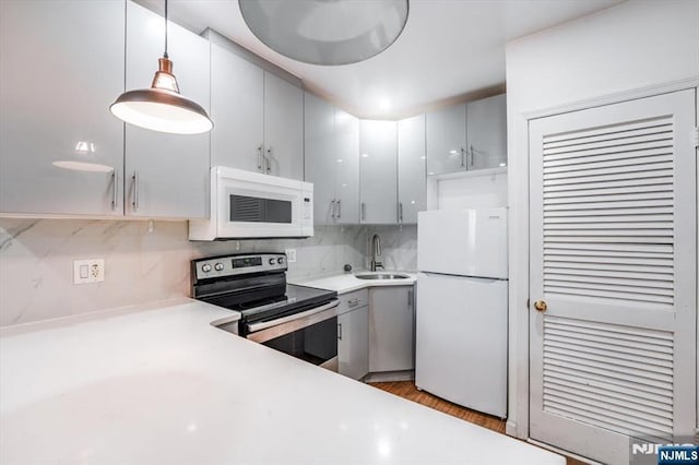 kitchen with pendant lighting, tasteful backsplash, sink, light hardwood / wood-style floors, and white appliances