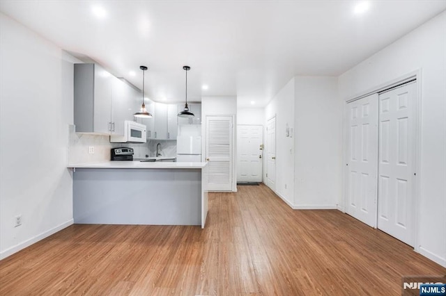 kitchen with white appliances, tasteful backsplash, light hardwood / wood-style floors, decorative light fixtures, and kitchen peninsula