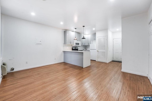 kitchen with white cabinetry, hanging light fixtures, kitchen peninsula, white appliances, and light hardwood / wood-style floors