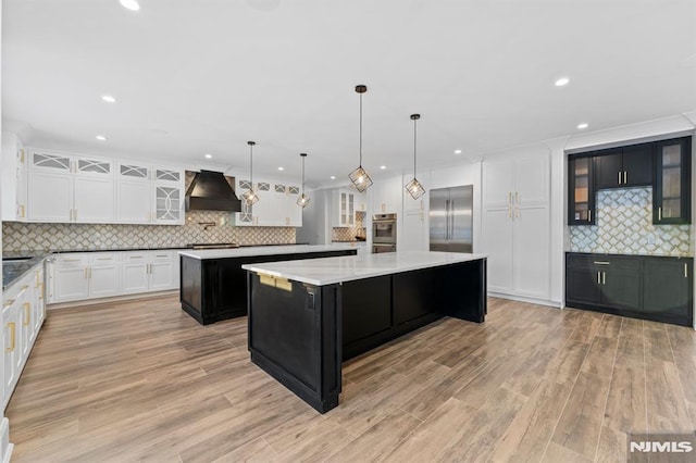 kitchen featuring pendant lighting, light hardwood / wood-style flooring, a large island, custom exhaust hood, and stainless steel built in fridge