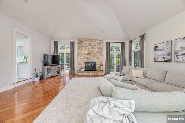 living room featuring high vaulted ceiling, wood-type flooring, and a stone fireplace