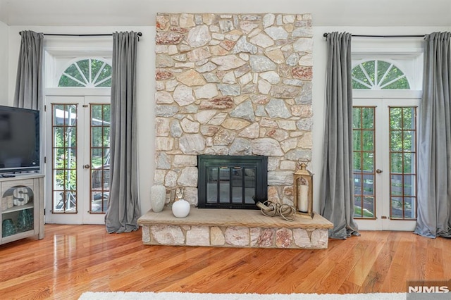 unfurnished living room featuring wood-type flooring, a stone fireplace, and french doors