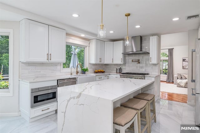 kitchen featuring appliances with stainless steel finishes, white cabinetry, sink, a kitchen island, and wall chimney exhaust hood