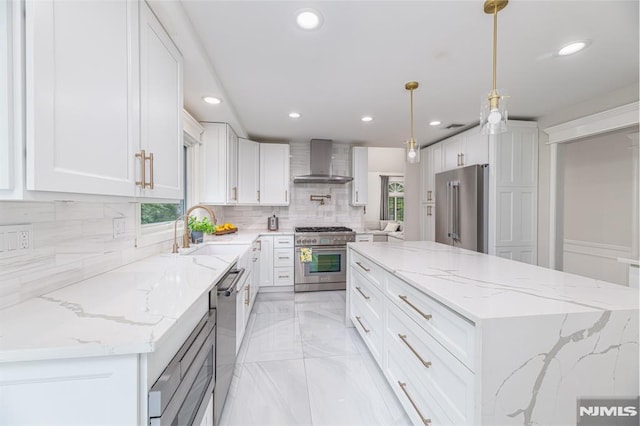 kitchen featuring premium appliances, white cabinets, decorative light fixtures, sink, and wall chimney exhaust hood