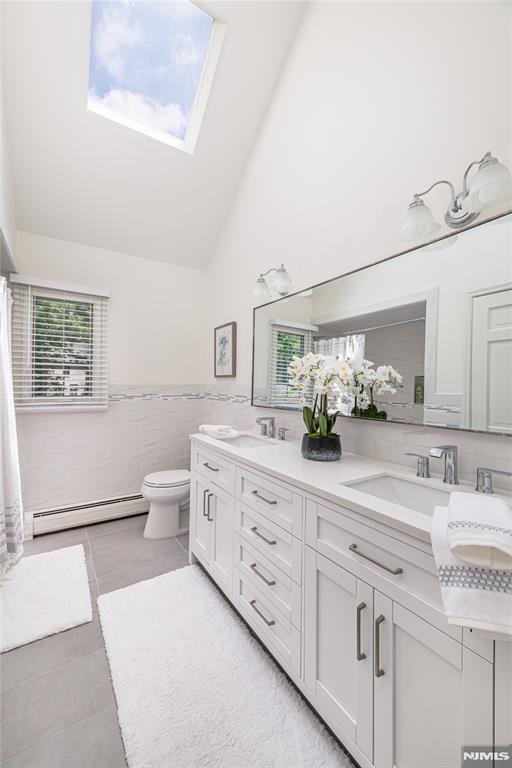 bathroom with tile patterned floors, a baseboard heating unit, tile walls, a skylight, and vanity