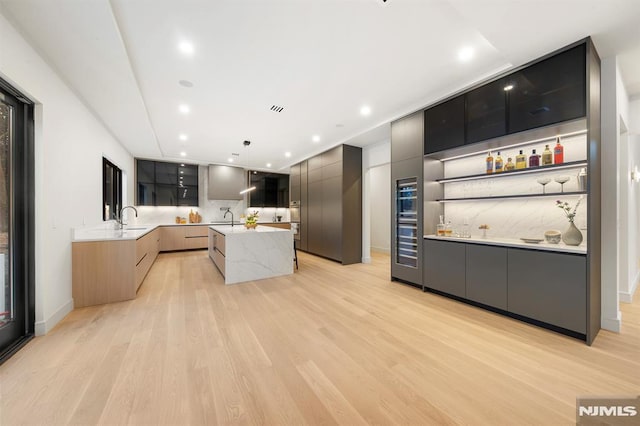 kitchen with a kitchen island with sink, sink, pendant lighting, and light brown cabinets