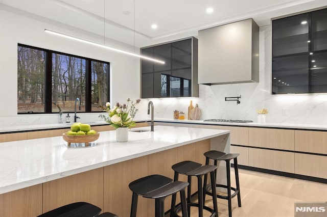 kitchen featuring stainless steel gas cooktop, sink, light stone counters, and a kitchen bar