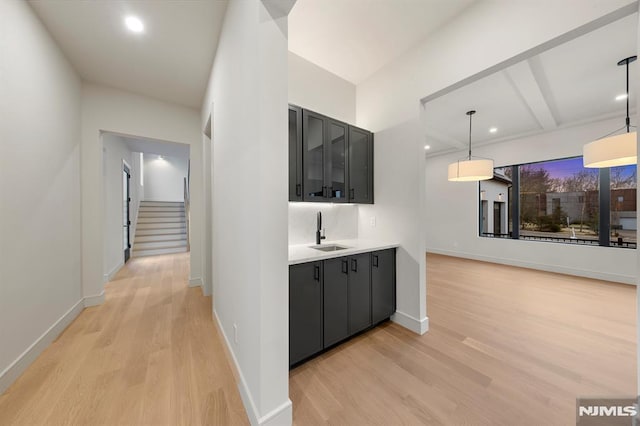 corridor with beam ceiling, light hardwood / wood-style floors, and sink