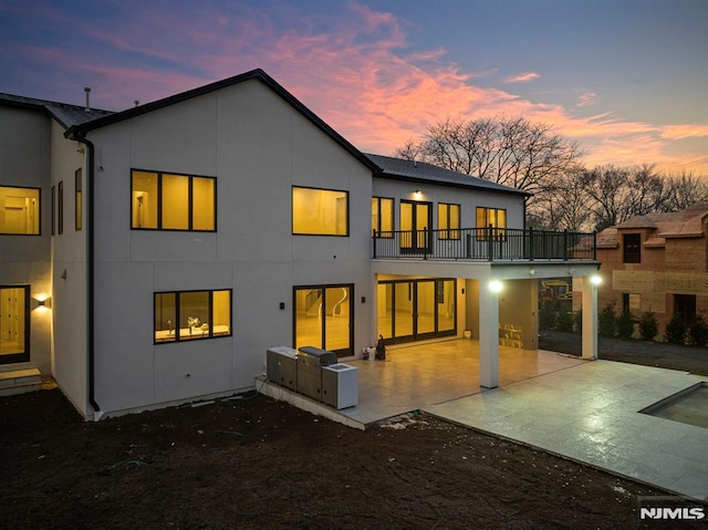 back house at dusk with a balcony and a patio area