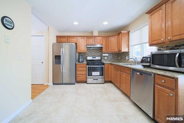 kitchen featuring light stone countertops, sink, backsplash, and stainless steel appliances