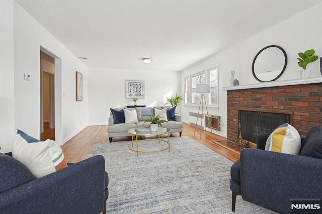 living room featuring a brick fireplace, radiator heating unit, and light wood-type flooring