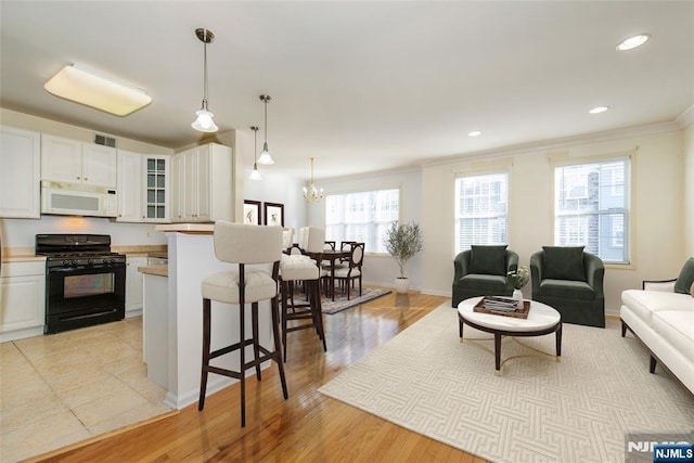 kitchen featuring black range with gas cooktop, white cabinetry, hanging light fixtures, ornamental molding, and a kitchen breakfast bar