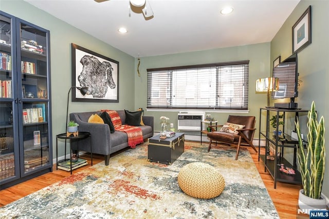 sitting room with a wall unit AC, hardwood / wood-style floors, and ceiling fan