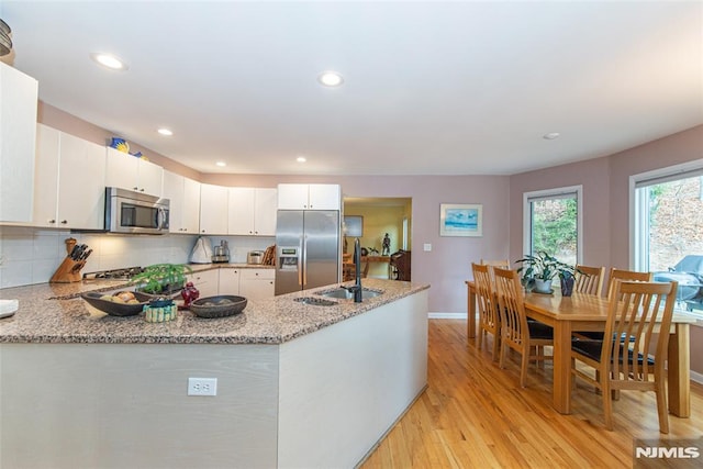 kitchen featuring light stone countertops, white cabinets, stainless steel appliances, light hardwood / wood-style floors, and kitchen peninsula