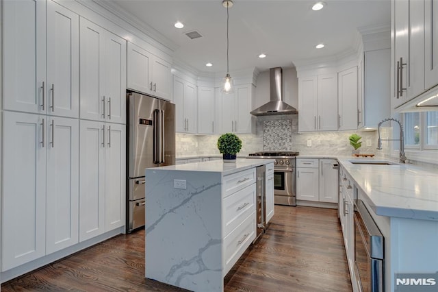 kitchen featuring premium appliances, hanging light fixtures, sink, white cabinets, and wall chimney range hood