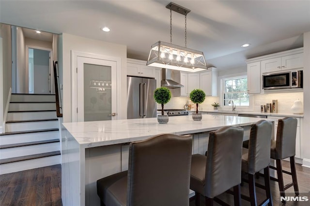 kitchen with white cabinetry, wall chimney range hood, appliances with stainless steel finishes, and a kitchen island