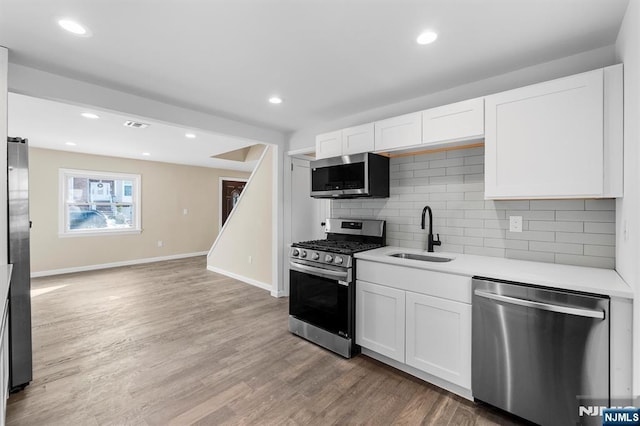 kitchen with white cabinetry, stainless steel appliances, light hardwood / wood-style floors, sink, and backsplash