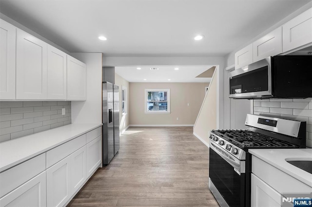 kitchen with white cabinets, light wood-type flooring, stainless steel appliances, and tasteful backsplash