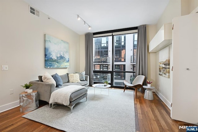 living room with visible vents, floor to ceiling windows, baseboards, and wood finished floors