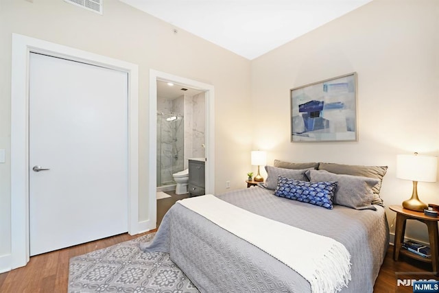 bedroom with ensuite bath, wood finished floors, and visible vents