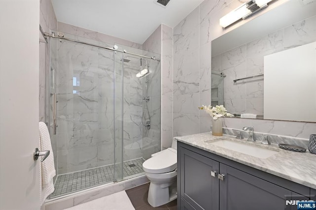 bathroom featuring vanity, tile walls, toilet, and a marble finish shower