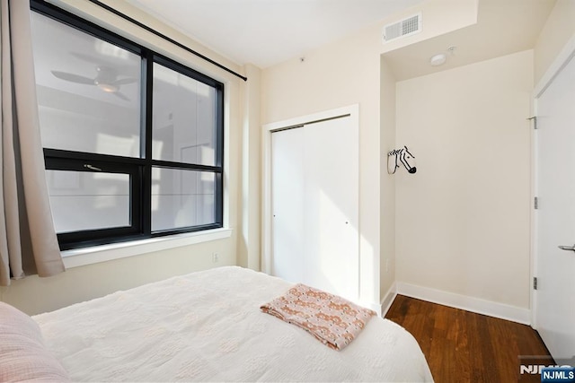 bedroom with a closet, visible vents, baseboards, and wood finished floors