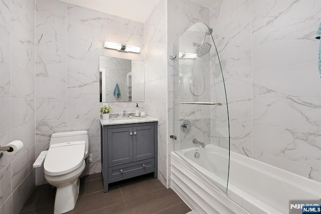 full bath featuring tile patterned floors, toilet, tile walls, washtub / shower combination, and vanity