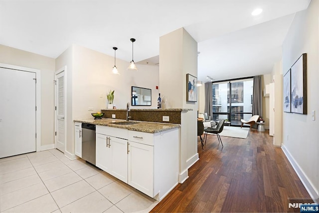 kitchen featuring light stone countertops, white cabinetry, a sink, pendant lighting, and stainless steel dishwasher