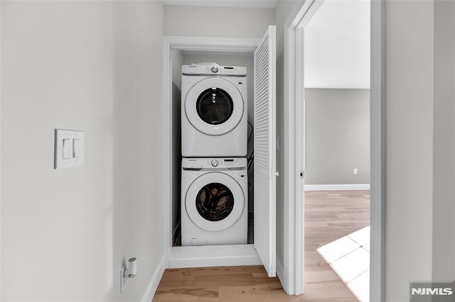 washroom with hardwood / wood-style flooring and stacked washer and clothes dryer