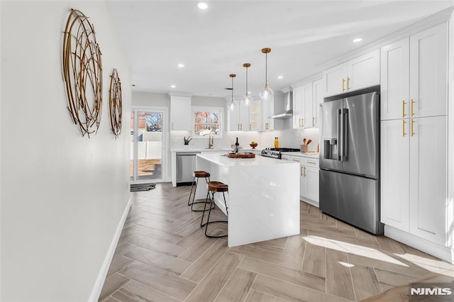 kitchen with a breakfast bar area, white cabinetry, a center island, appliances with stainless steel finishes, and wall chimney range hood