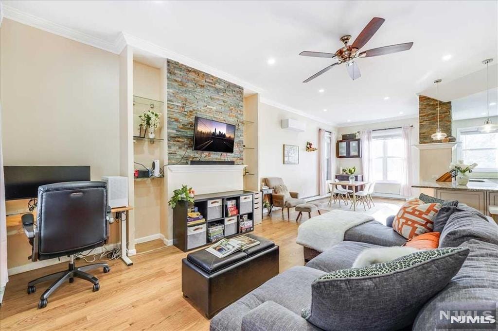 living room featuring light wood-type flooring, ceiling fan, an AC wall unit, and crown molding