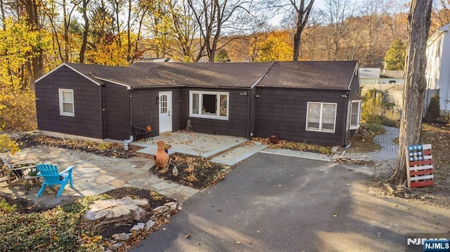 ranch-style house with a shingled roof and a patio