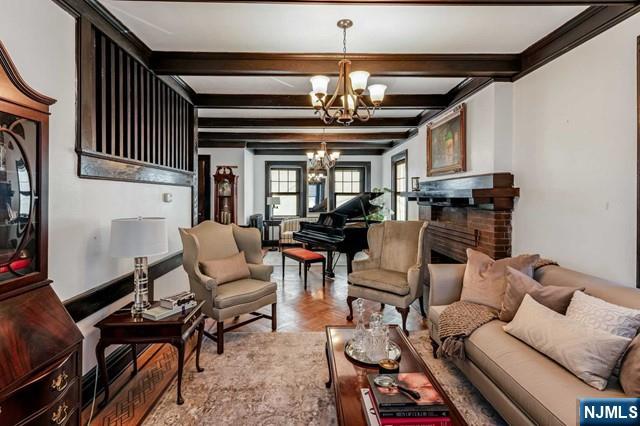 interior space featuring beam ceiling, a chandelier, a fireplace, ornamental molding, and light parquet flooring