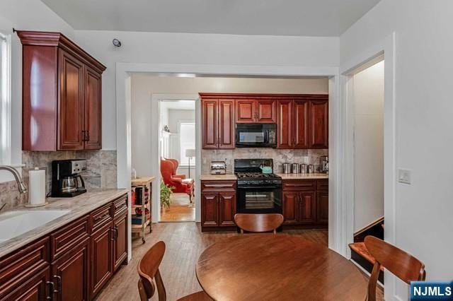 kitchen featuring wood-type flooring, sink, backsplash, black appliances, and plenty of natural light