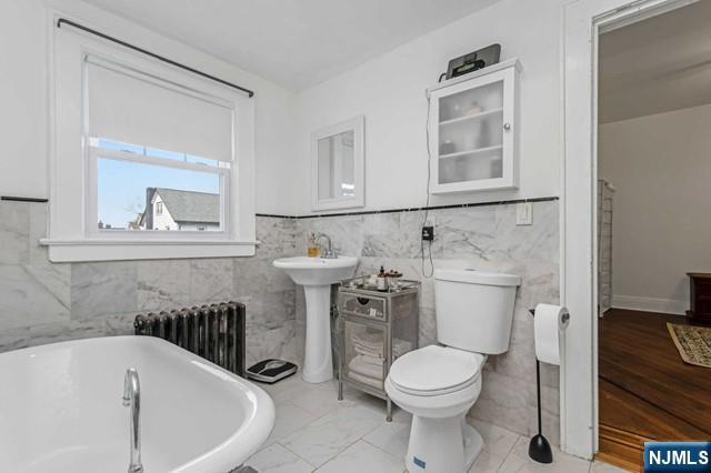 bathroom with toilet, a bath, radiator, and tile walls