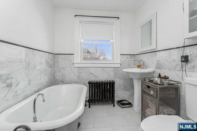 bathroom featuring tile walls, a bath, radiator heating unit, and toilet