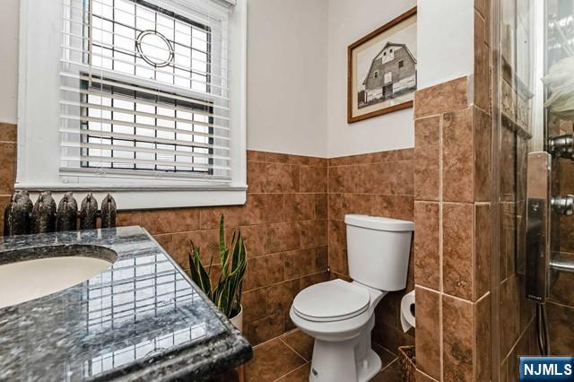 bathroom featuring walk in shower, tile walls, and toilet