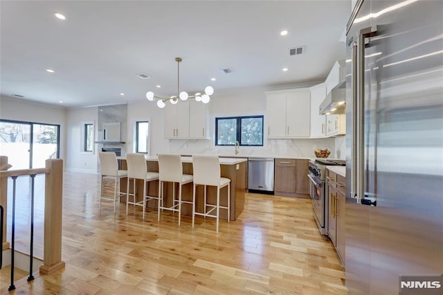 kitchen featuring high quality appliances, white cabinets, a center island, and hanging light fixtures