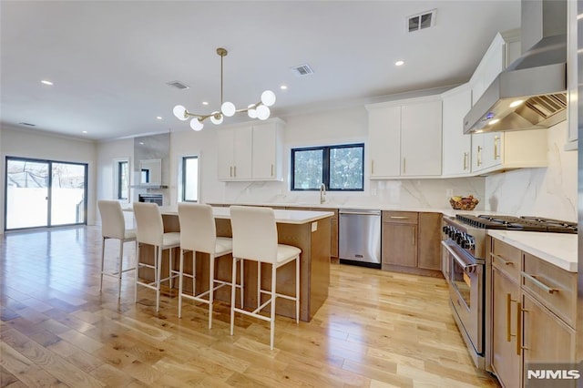 kitchen featuring appliances with stainless steel finishes, a center island, white cabinetry, wall chimney range hood, and tasteful backsplash