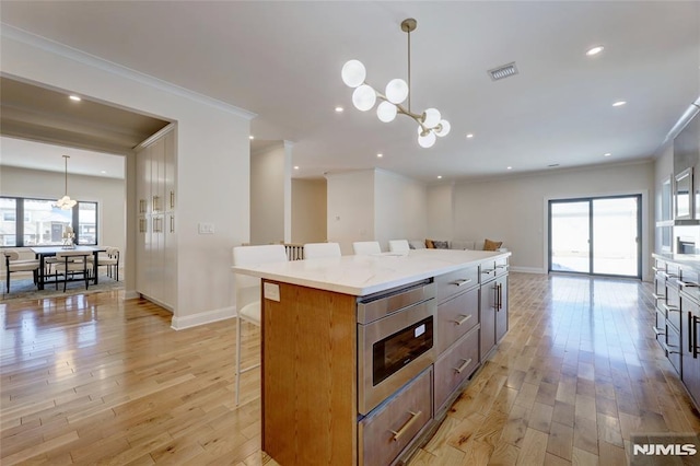 kitchen featuring a center island, crown molding, a chandelier, light wood-type flooring, and pendant lighting