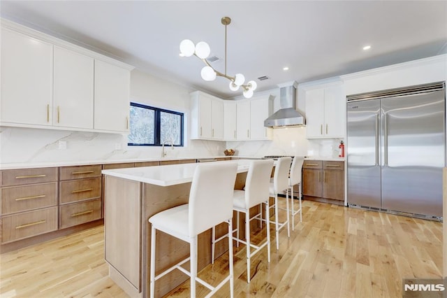 kitchen with pendant lighting, white cabinetry, stainless steel built in fridge, and wall chimney exhaust hood