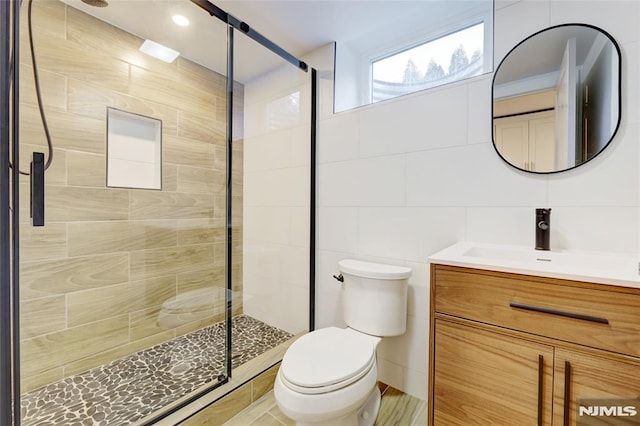 bathroom with tile walls, an enclosed shower, vanity, and toilet